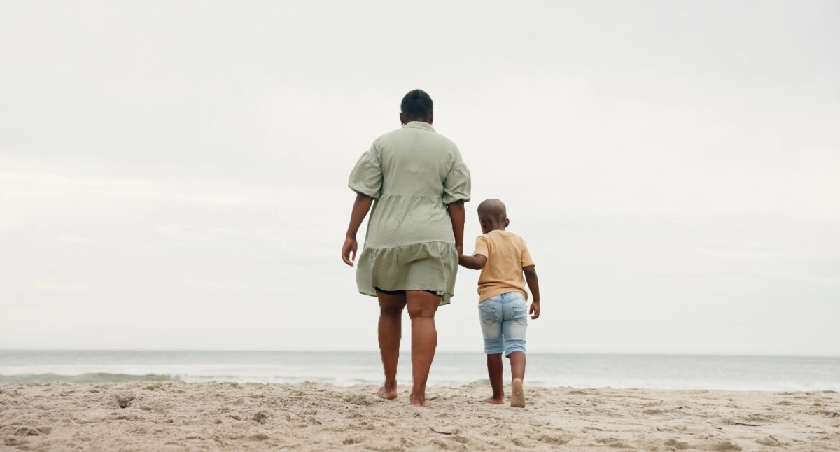 woman and child holding hands walking on a beach towards the water