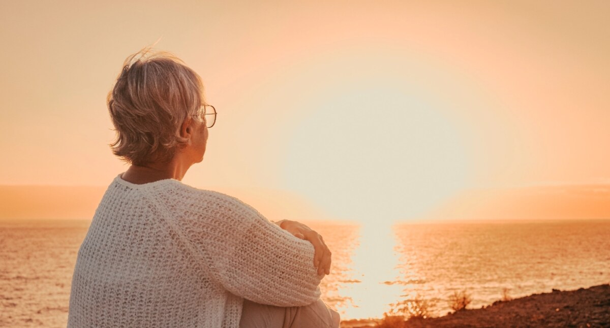 woman sitting on the shore looking out at a sunset